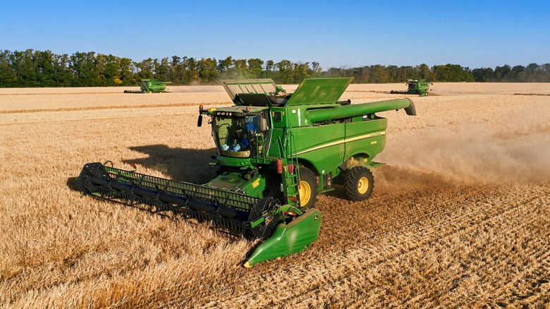 Three John Deere harvesters driving through a field.