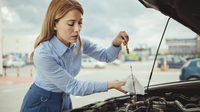 Woman checking motor oil levels with dipstick.
