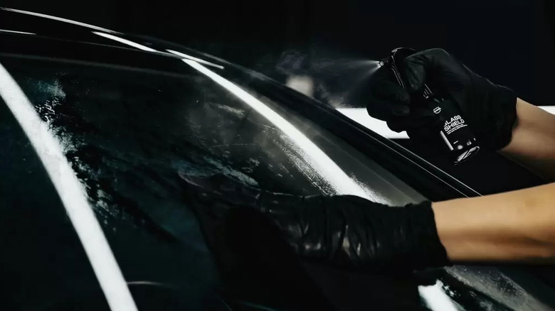 Gloved hands apply a water-repellent spray to a car windshield