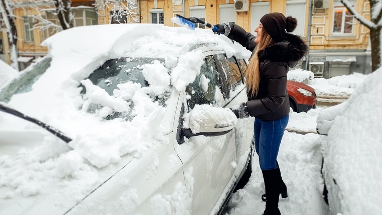 Woman removing snow from a car with a brush