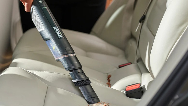a closeup image of someone using the ryobi handheld vacuum on a car seat