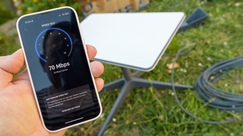 Hand holding phone with Starlink speed test with Starlink dish in the background