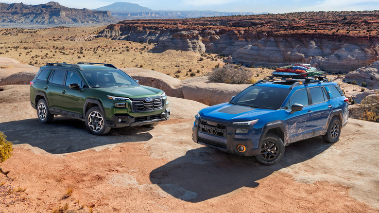 A duo of 2026 Subaru Outbacks on a rock formation, green one on the left, blue Wilderness on the right