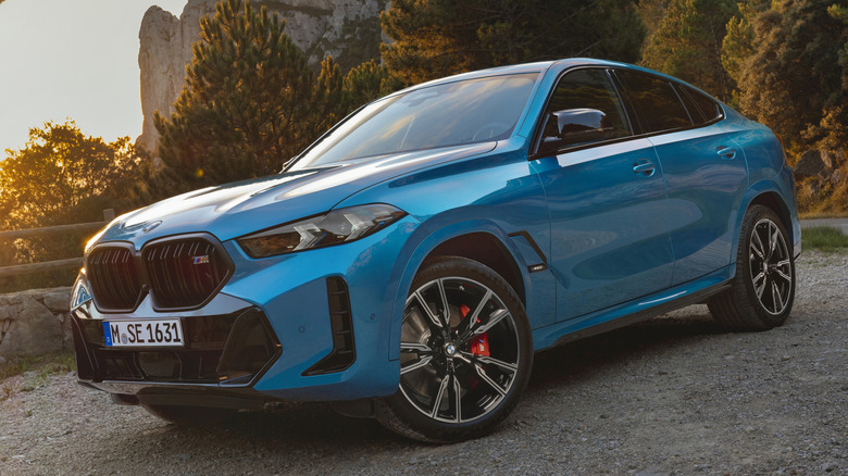 Blue 2025 BMW X6 M60i parked in gravel in a mountainous area