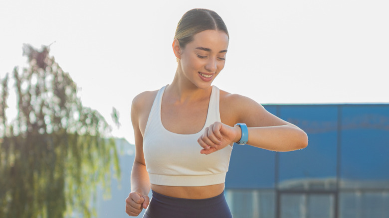 A woman in park in running gear looking at the smart watch on her wrist