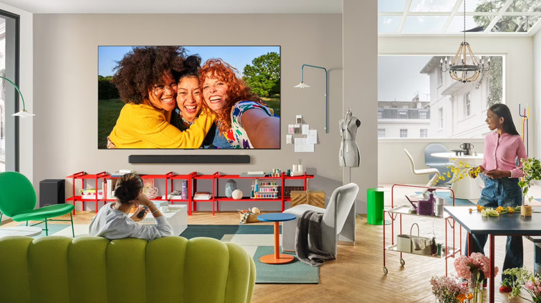 Two people in a bright studio apartment with an LG C5 TV hanging on a wall