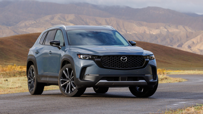 Front 3/4 view of a grayish blue Mazda CX-50 against a mountainous backdrop