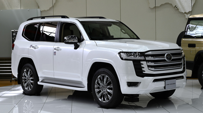 White 2021 Toyota Land Cruiser on showroom floor, front-right 3/4 view.