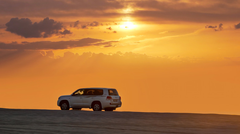 100-series Toyota Land Cruiser driving in the desert at sunset.