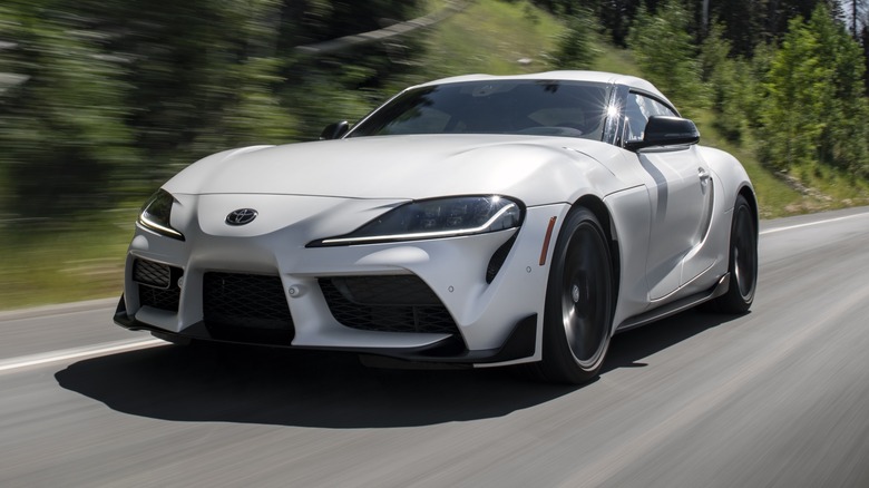Matte White 2023 Toyota GR Supra driving on a road with dense vegetation in the background