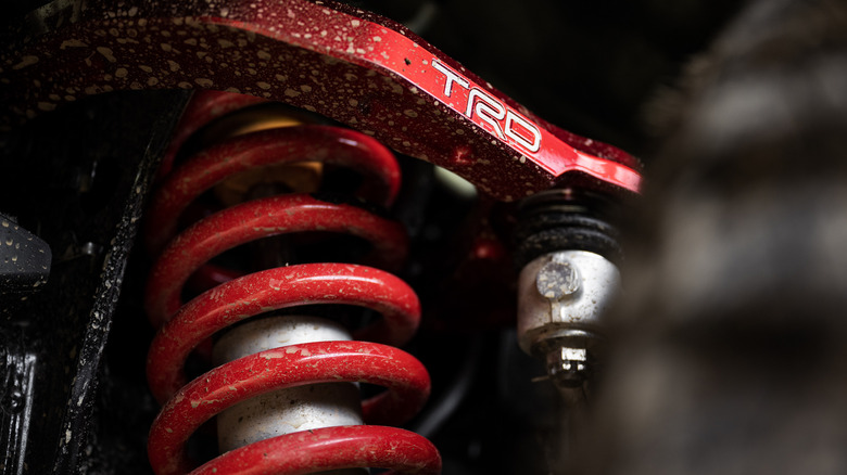 A mud and dust covered red coil-over-shock suspension on a Tacoma TDR Pro