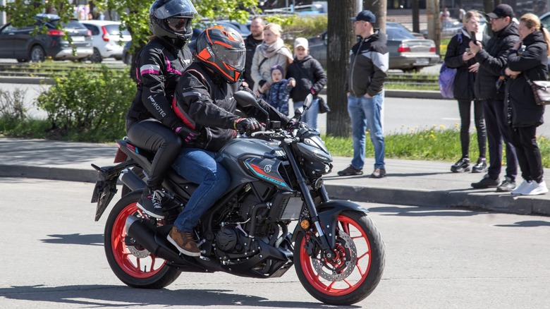 A couple rides a Yamaha MT-03 past a group of onlookers.