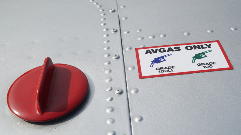Aircraft closed fuel port with "AVGAS ONLY" placard showing 100LL and 100 grades with colored nozzles.