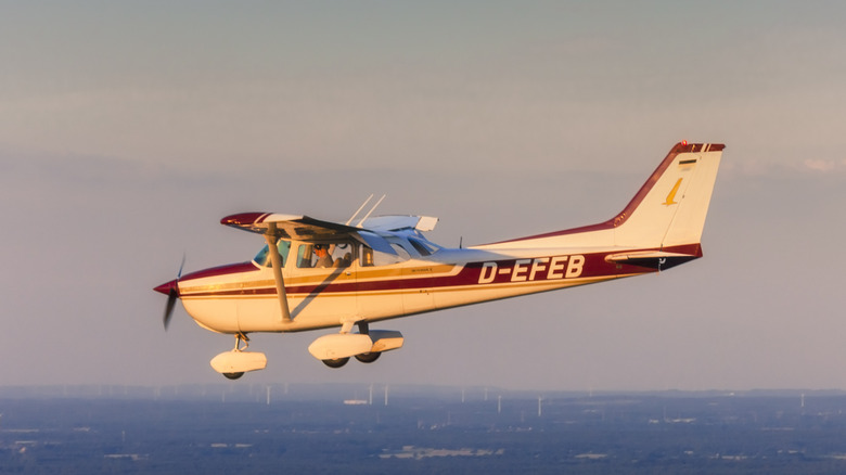 Cessna 172 with tail number D-EFEB flying over flat developed landscape at sunset, left-side view.