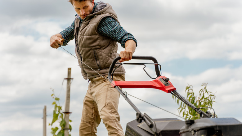 Man pulling lawn mower cord on cloudy day