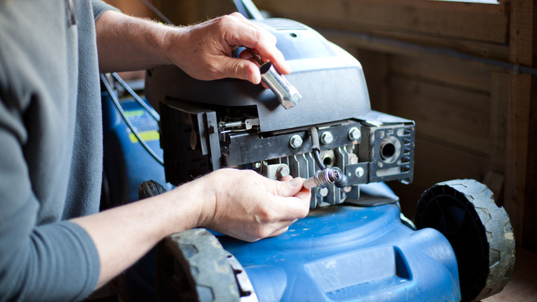 A man inspects the spark plug on his lawn mower