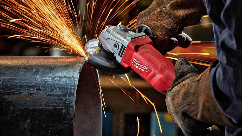 A welder using a Milwaukee grinder to cut through a metallic material