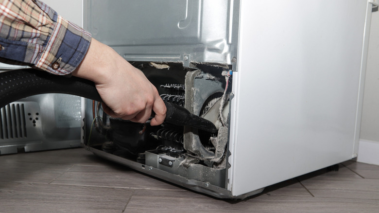 Male hand vacuuming refrigerator condenser and internal components after removing back cover