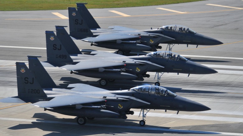 A trio of F-15 fighter jets on the tarmac ready for takeoff.