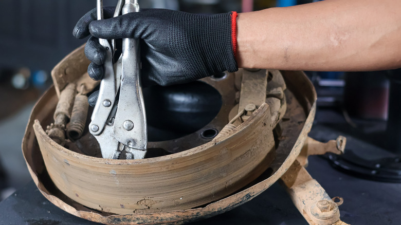 Person wearing a black latex glove using a pair of Vise-Grips to repair a drum brake backing plate