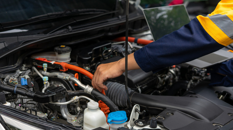 mechanic working under hood of car with laptop