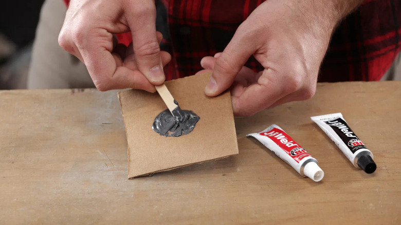 A shot of a pair of hands mixing J-B Weld on cardboard