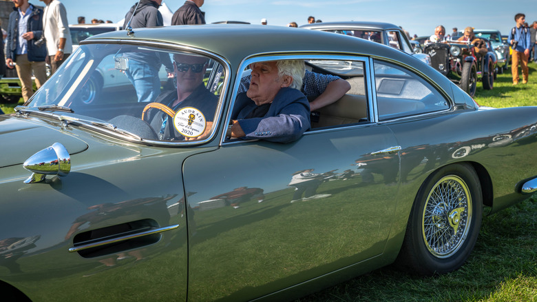 Jay Leno sitting in an Aston Martin at an Audrain Concours event.