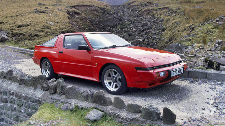 A red Mitsubishi Starion (or Chrysler Conquest) pictured parked on a rocky road on the side of a hill.