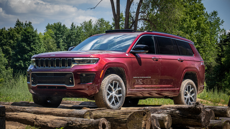 Red 2021 Jeep Grand Cherokee stands in front of trees and behind wooden logs