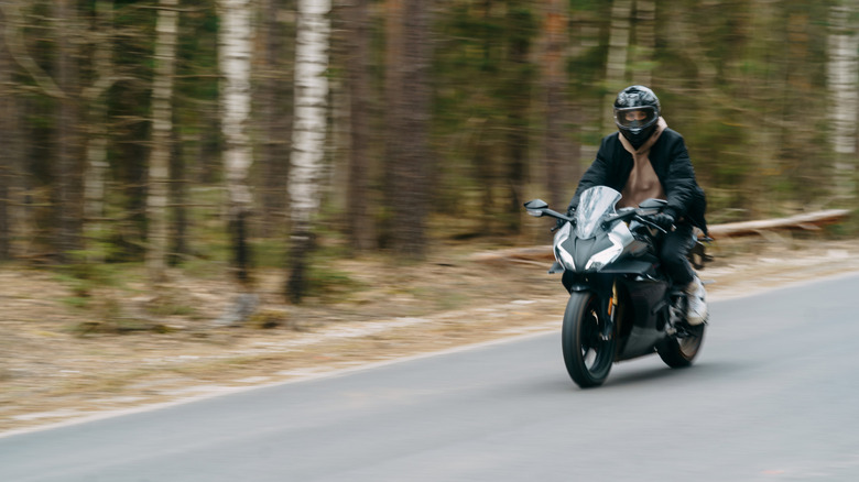 Helmeted motorcycle rider on wooded road