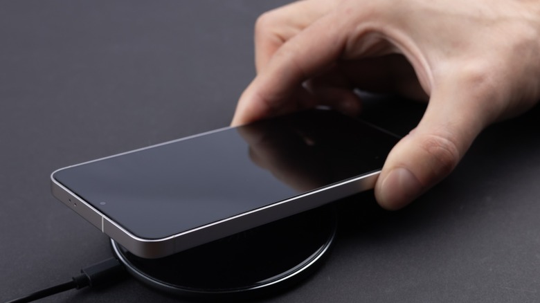 A hand placing a phone on a wireless charger against a dark gray surface