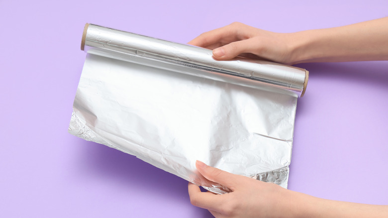 Person stretching aluminum foil on purple backdrop
