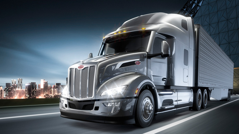 Front 3/4 studio render of a grey Peterbilt 579 driving through the city at night.