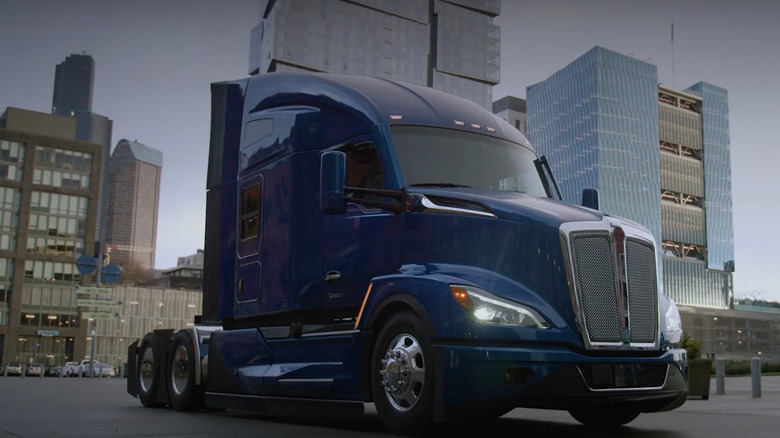 Blue Kenworth T680 parked with tall buildings in the background