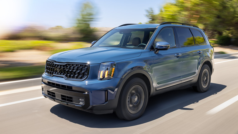Blue 2025 Kia Telluride driving on road, front 3/4 view