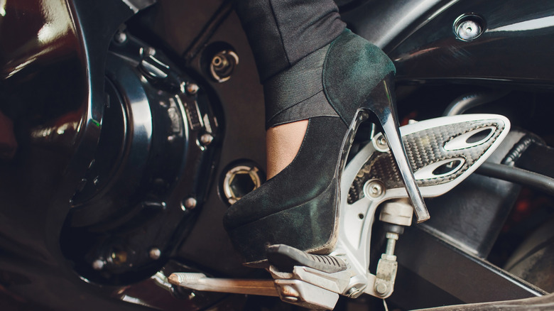 Foot in high-heeled shoes on a motorcycle kickstart lever