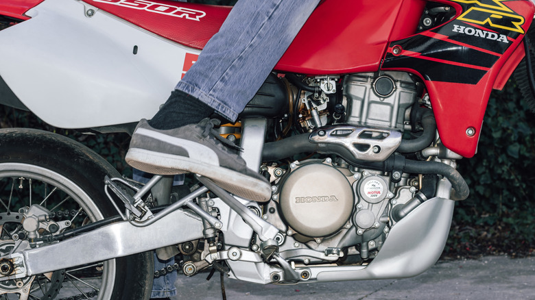 Person kickstarting Honda XR 650 R motorcycle in jeans and sneakers