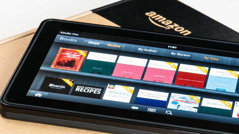 A Kindle tablet displaying different book titles while laying on top of an Amazon-branded box.