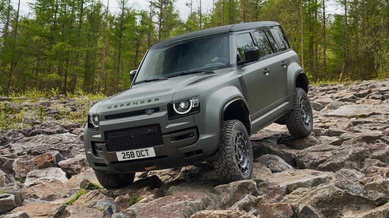 Land Rover Defender Octa rock crawling with trees in the background, front 3/4 view