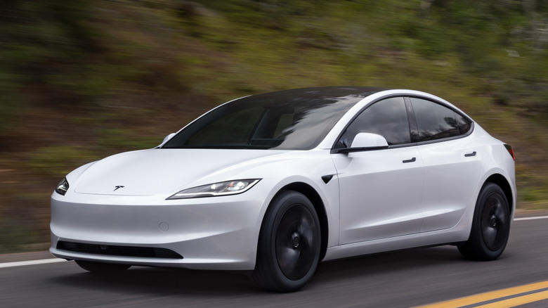 A front 3/4 view of Tesla Model 3 driving on a road in a forested setting