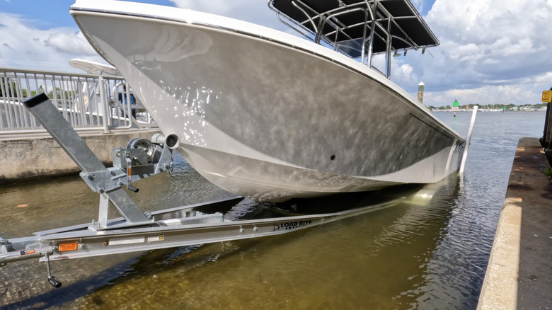 A white boat is unloading off a ramp into a water body