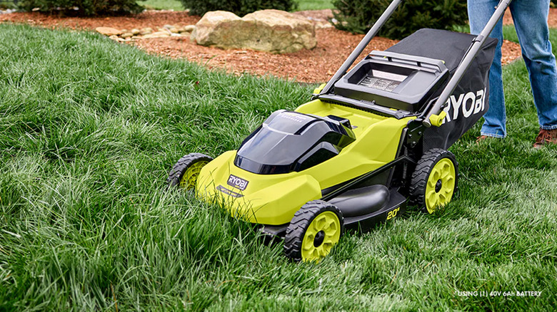 A man mowing a lawn with a Ryobi lawn mower.