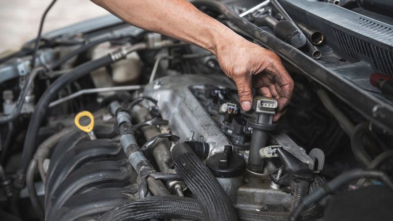 person replacing ignition coil in engine