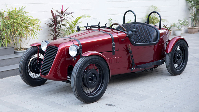 MAroon Austin Arrow EV roadster parked on flags at a showroom
