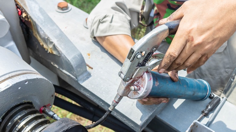 A mechanic applies grease with a pistol-grip grease gun.