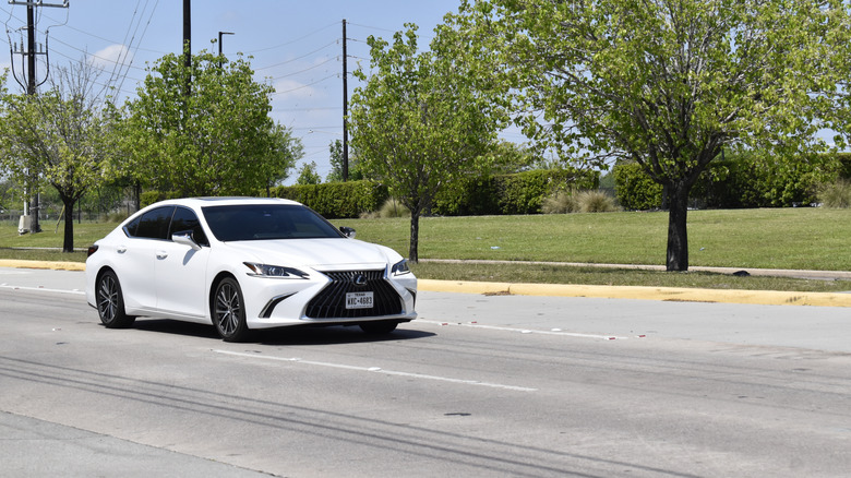 A white Lexus ES driving along a road dotted with trees.