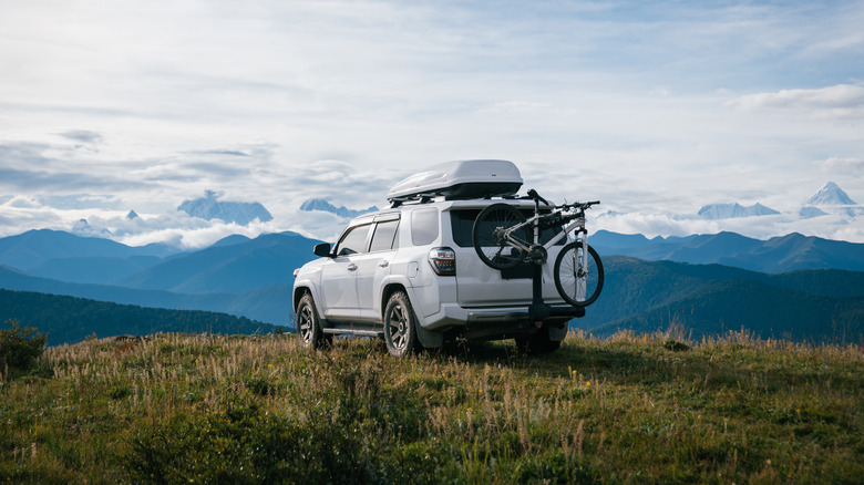 A white Toyota 4Runner with mounted roof rack overlooking mountains.