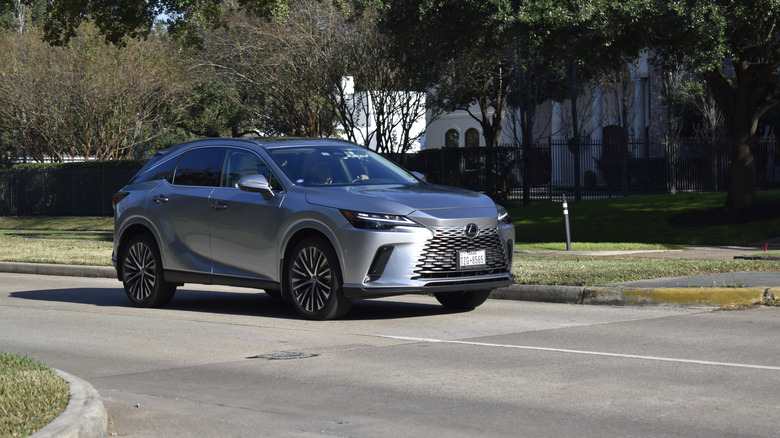 A silver 2026 Lexus RX driving along a small road.