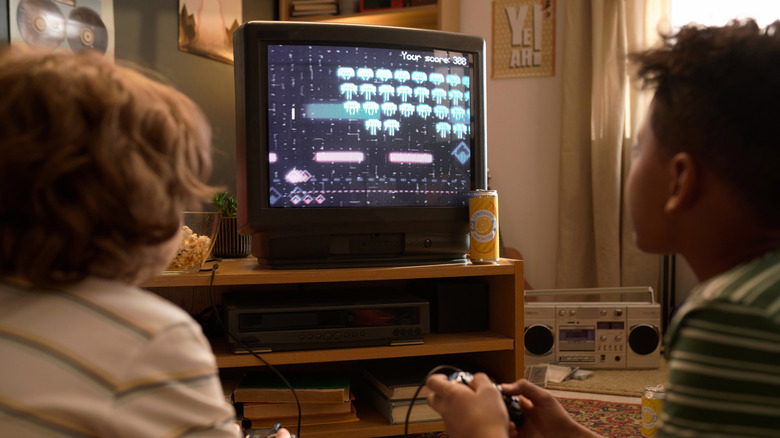 An old CRT TV showing space invaders, with two children gaming.