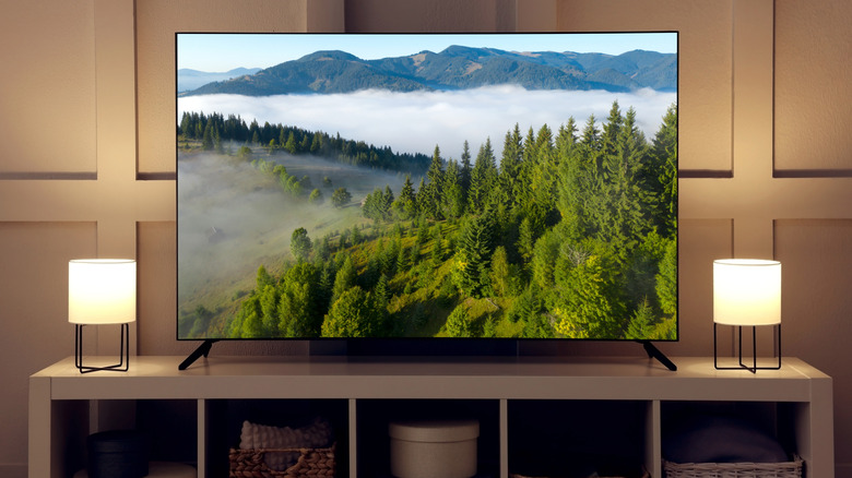 Smart TV sitting on TV stand in living room area, soft lights on either side